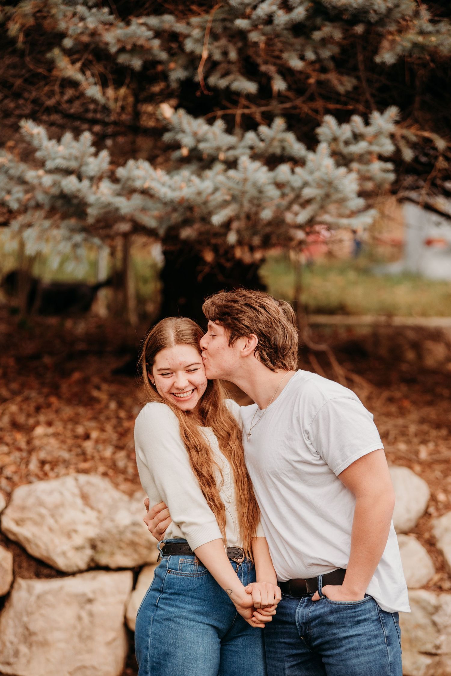 A romantic couple sharing a tender moment under blooming cherry blossoms near a stone wall.