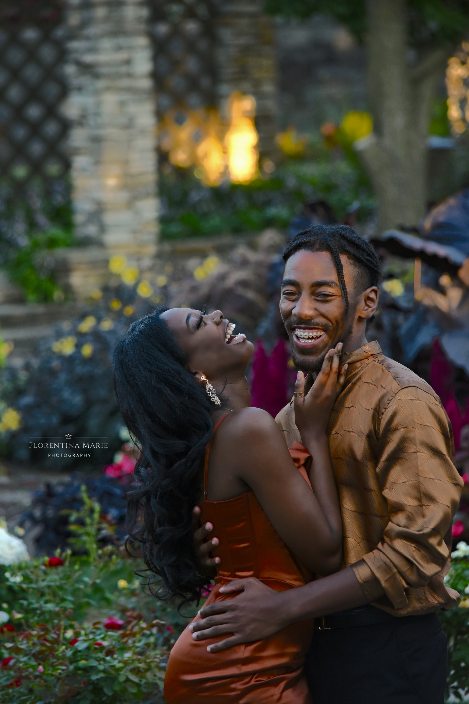 A joyful couple shares a tender moment while laughing together in a garden setting at sunset.