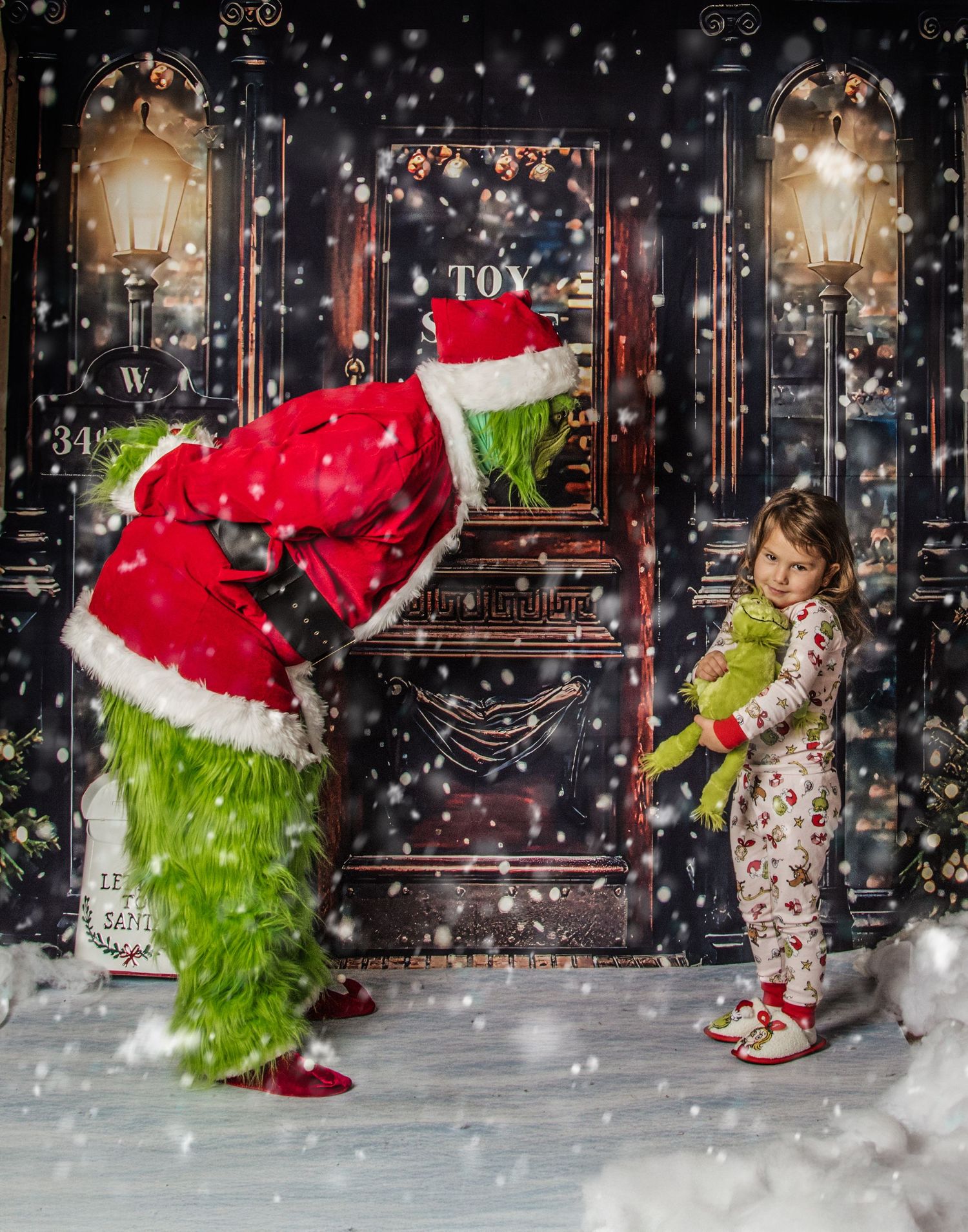 A furry green character in Santa suit bends down to interact with a child in Christmas pajamas by a snowy door at night.