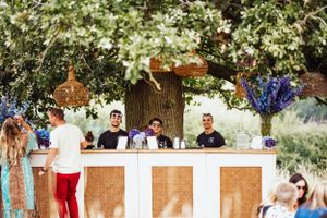 Outdoor bar setup with wooden panels and floral decorations serving guests at a garden event.