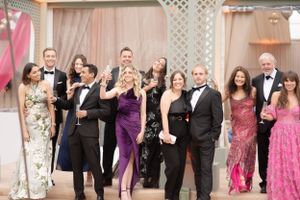 A group of elegantly dressed party guests in formal attire laughing and celebrating at an event with a lattice backdrop.