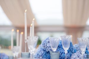 Elegant white candles and crystal glassware arranged with delicate blue floral decor on a formal dining table.