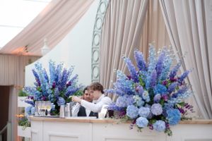 Elegant wedding bar setup with stunning blue and purple floral arrangements against white draped backdrop.