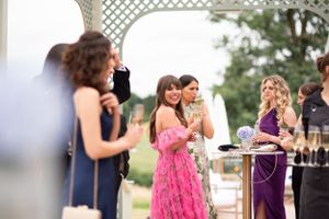 Guests in formal attire gather at an outdoor reception near a white lattice arch with drinks and refreshments.