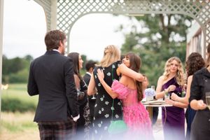 Wedding guests enjoying drinks and conversation at an outdoor reception with lattice gazebo in the background.