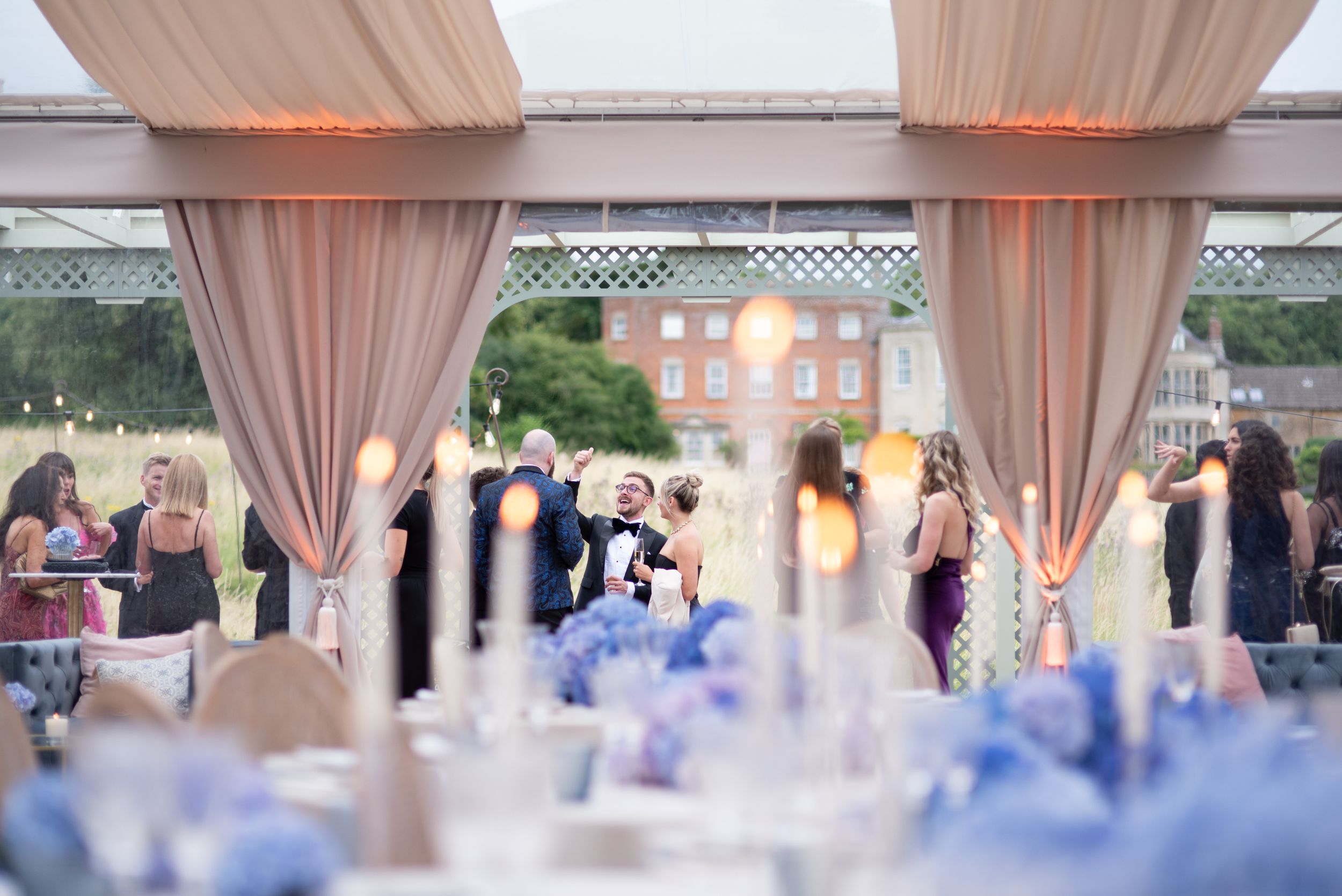 Wedding reception venue decorated with sheer drapes and blue table settings, with guests mingling in soft lighting.