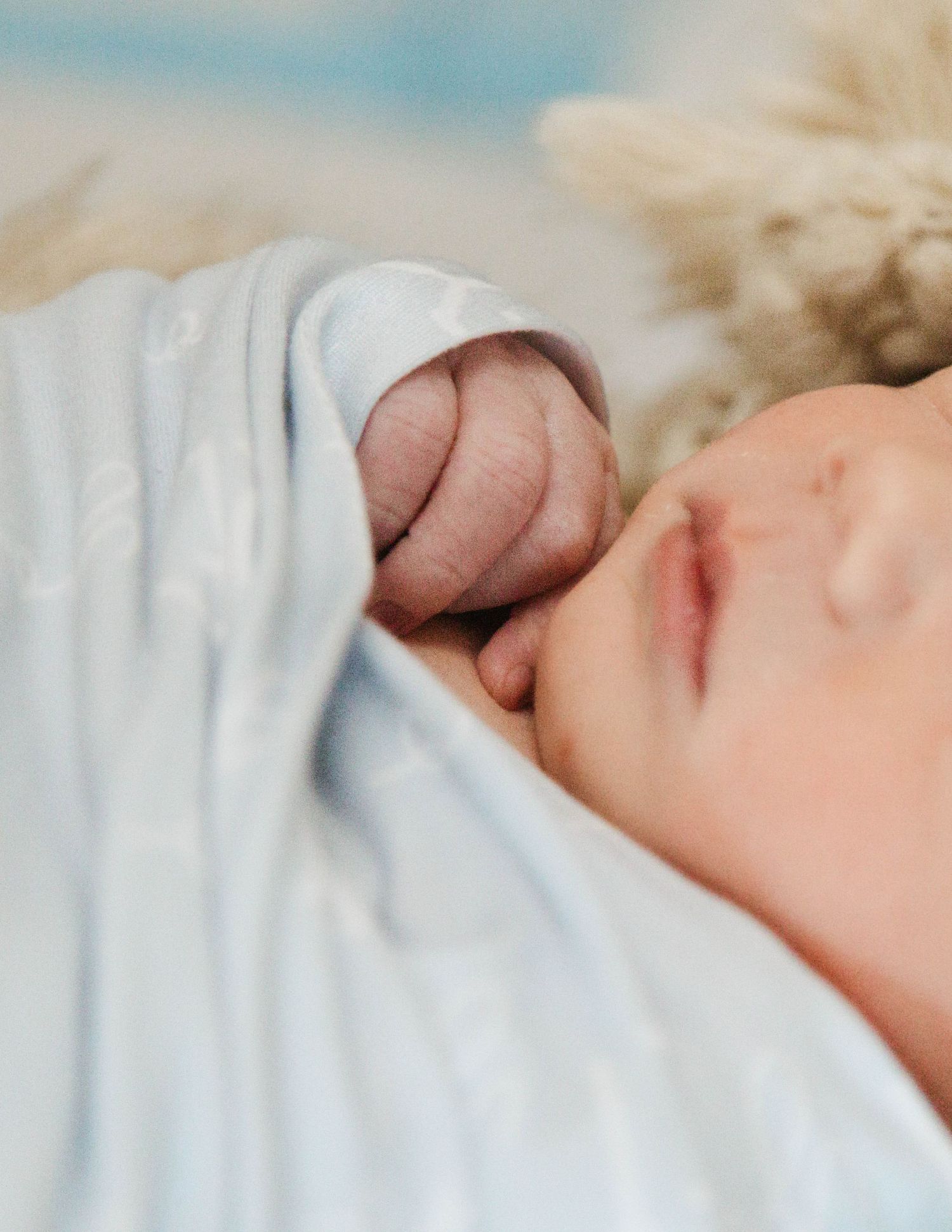 A tender moment between parent and newborn baby near a window with a rainbow decoration visible in the background.