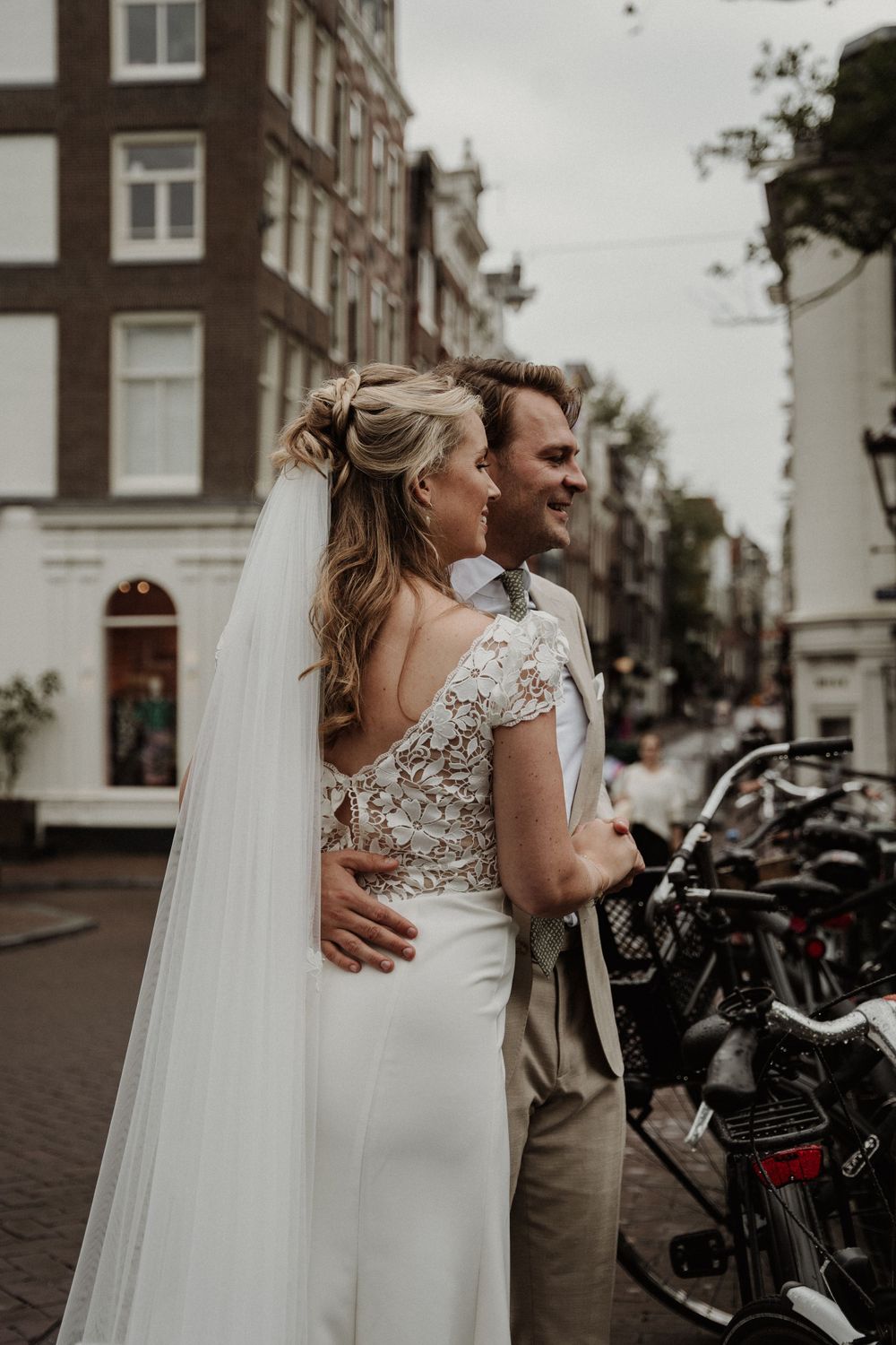 A romantic wedding couple embraces on a charming Amsterdam street lined with bicycles and historic buildings.