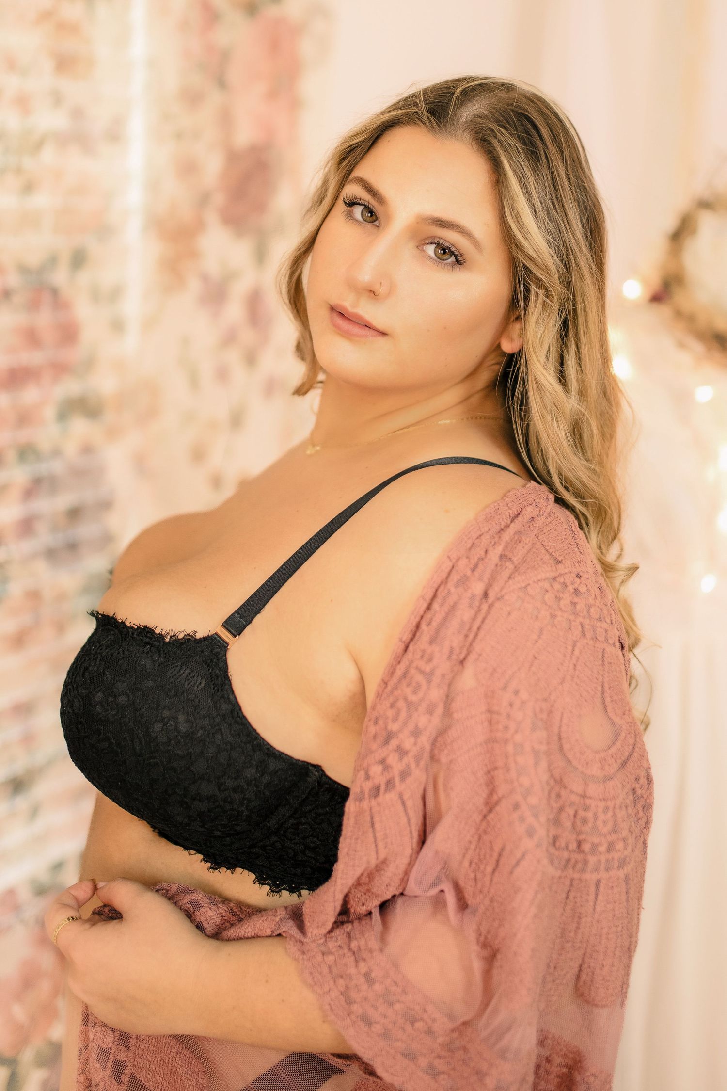 Curvy blonde woman in black lingerie and lace cardigan in pastel studio boudoir session, elegant and empowering, phot by Tasha Cannaday.