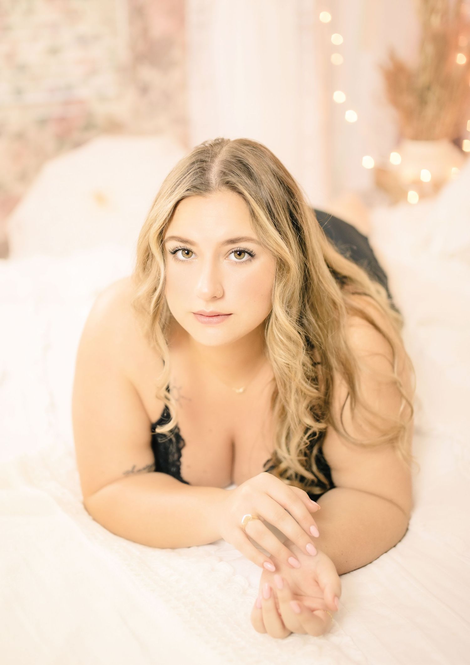 Empowering boudoir photo of curvy blonde woman in black lingerie, kneeling in pastel-toned studio for self-love session.