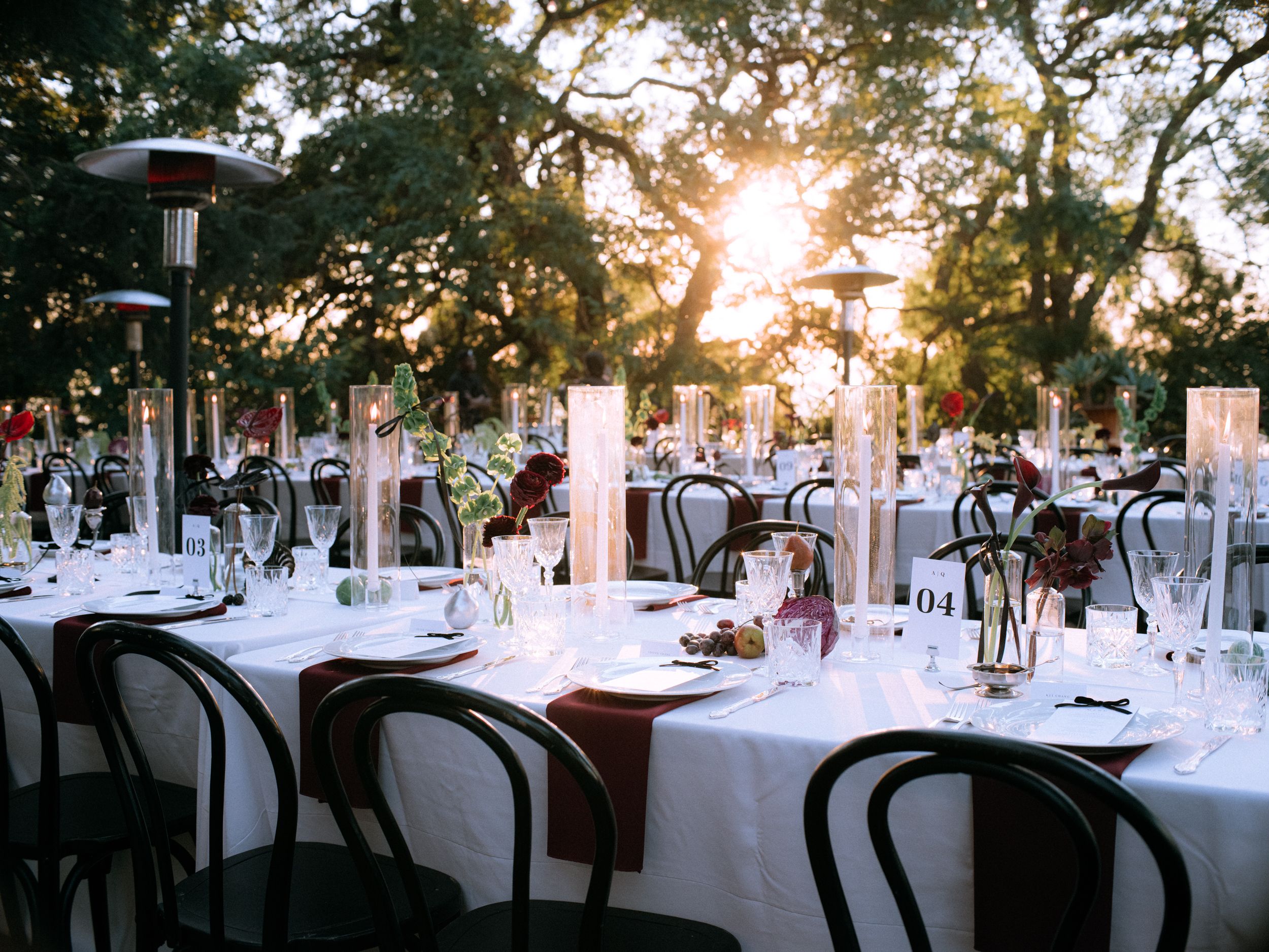 Elegant outdoor wedding reception tables set with white linens under string lights at sunset.