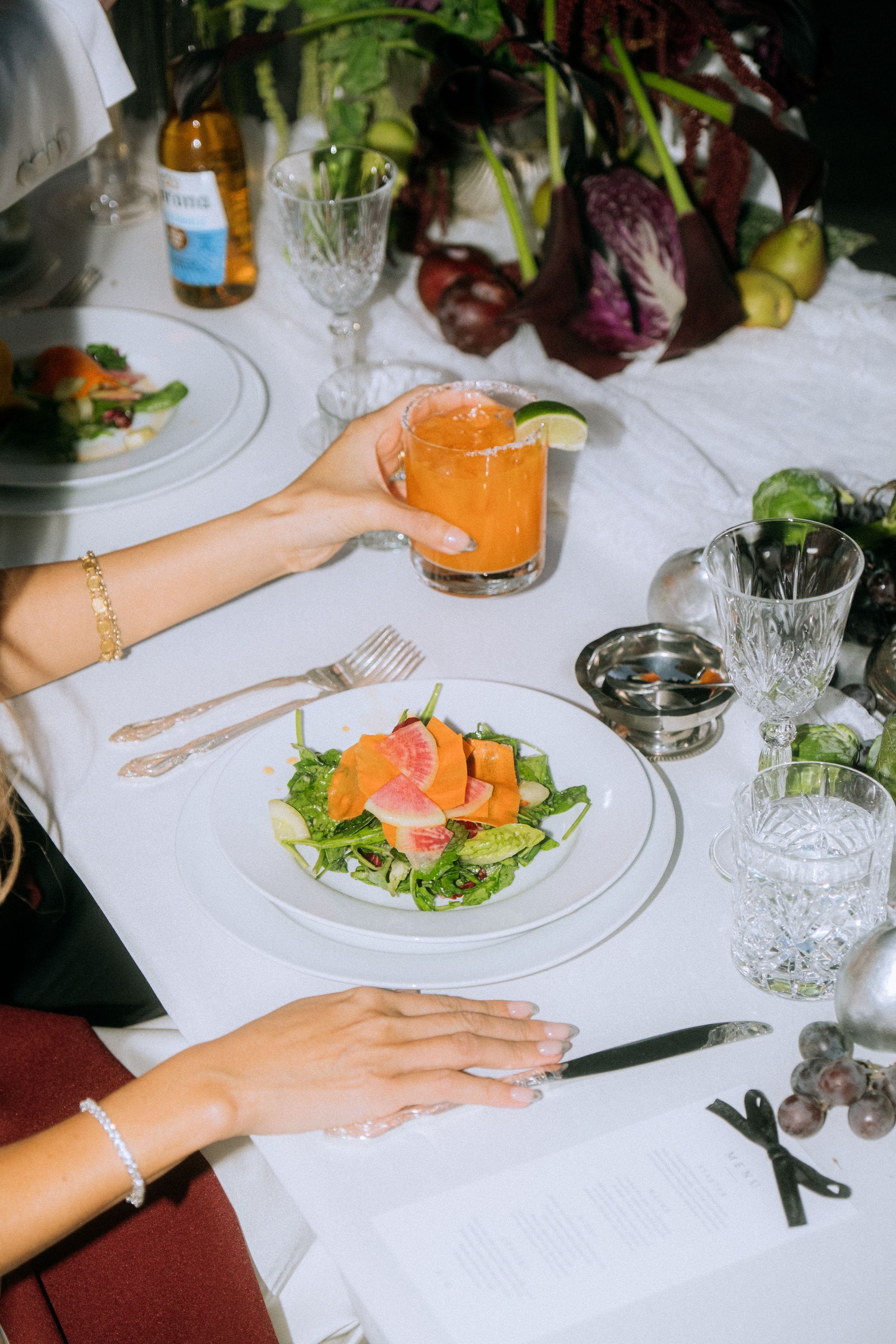 Elegant table setting with fresh salad and cocktail on white tablecloth with crystal glassware.