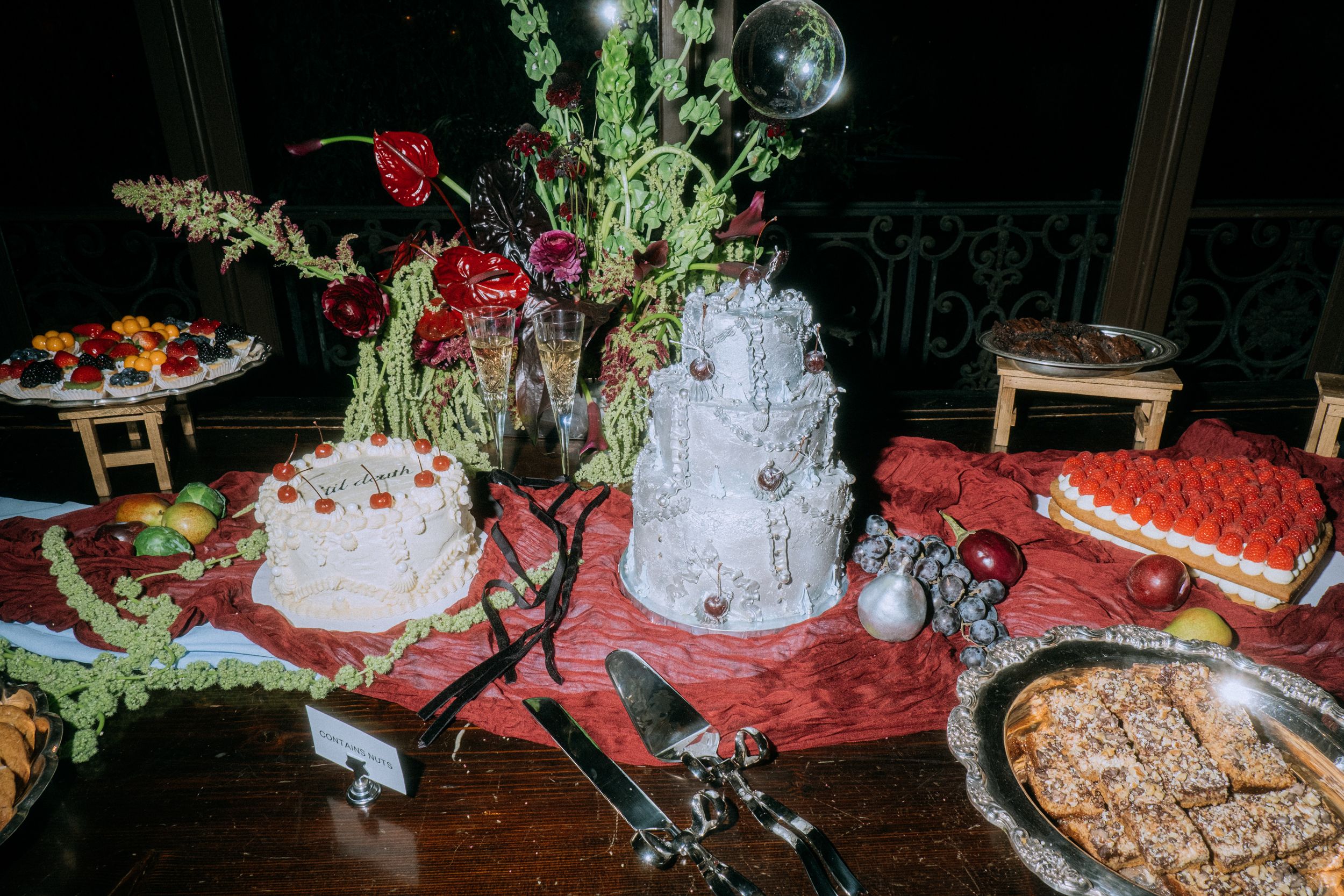 Elegant dessert table with multiple cakes, floral arrangements and treats at an evening event.
