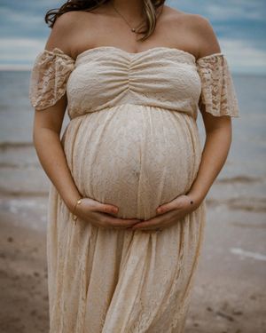 Maternity woman on beach holding belly for maternity pictures. Captured by Maryland Photographer Mallory Bramlett.