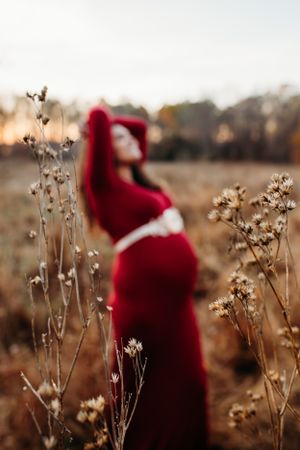 Maternity woman in red dress in field for maternity pictures. Captured by Maryland Photographer Mallory Bramlett.