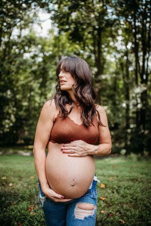 Maternity woman holding belly outdoors for maternity shoot. Captured by Maryland maternity Photographer Mallory Bramlett.