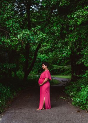 Maternity woman standing between trees for maternity photoshoot. Captured by Maryland Photographer Mallory Bramlett.