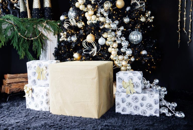Christmas presents wrapped in cream and patterned paper beneath an ornate white and gold decorated tree.