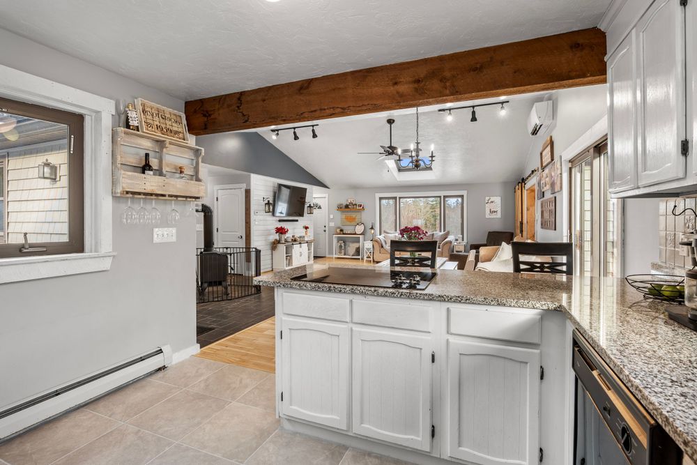 Rustic-modern kitchen with exposed beam, white cabinets, and granite countertops.