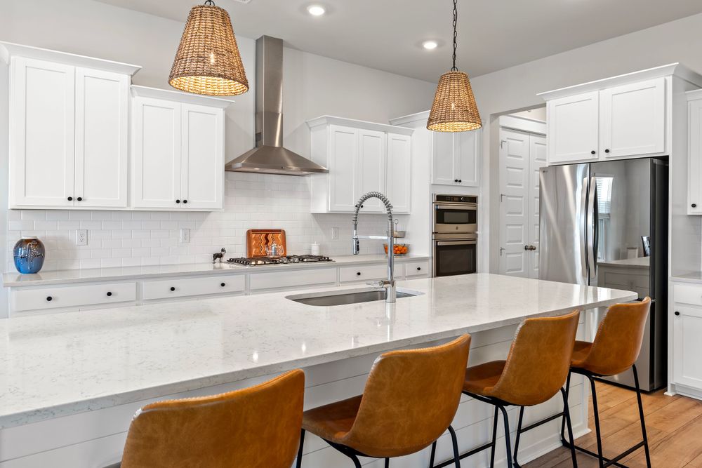 Modern white kitchen with rattan pendant lights, stainless appliances and brown leather barstools at marble island.