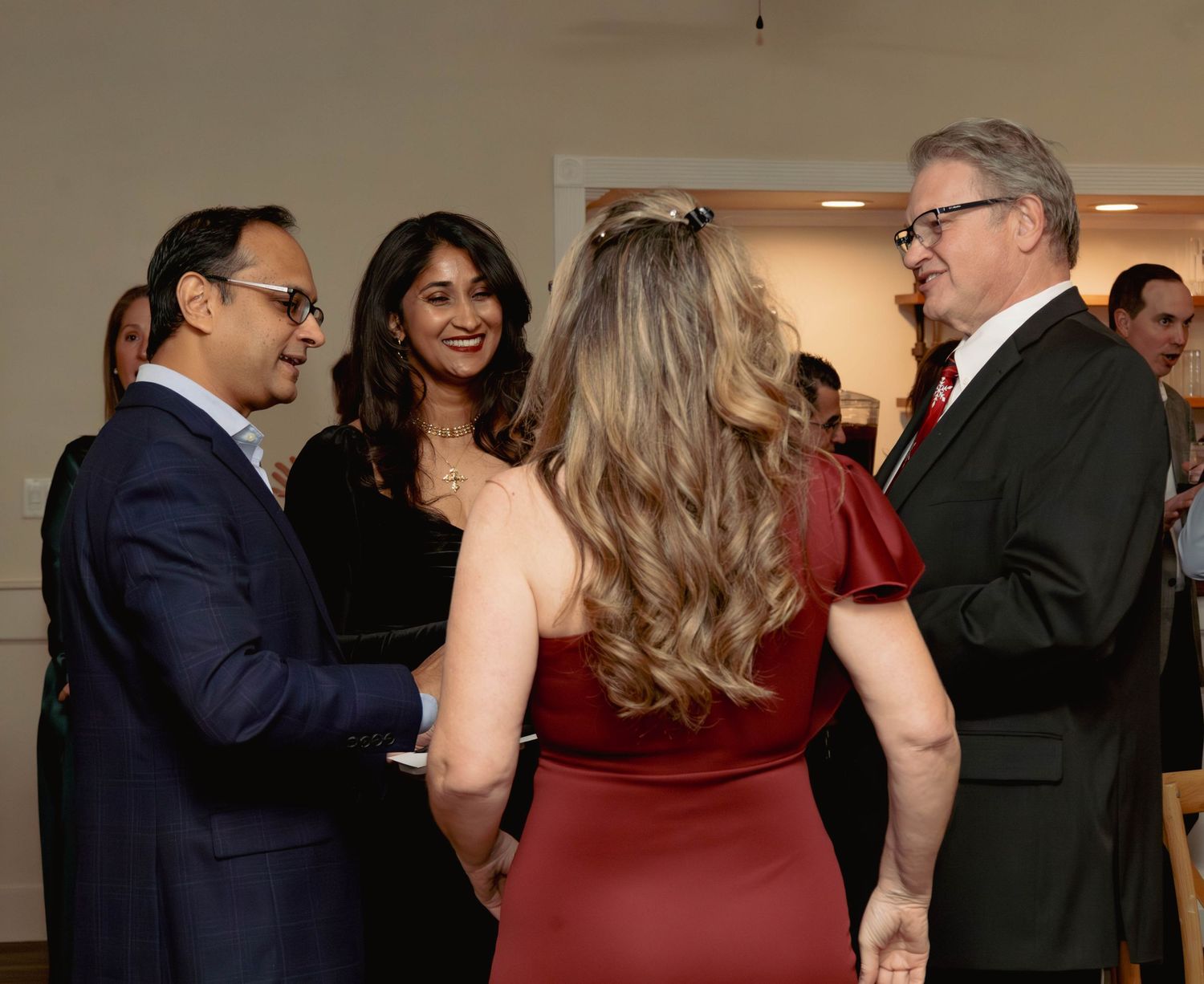 Four guests in formal attire engage in conversation at an upscale social gathering or reception event.