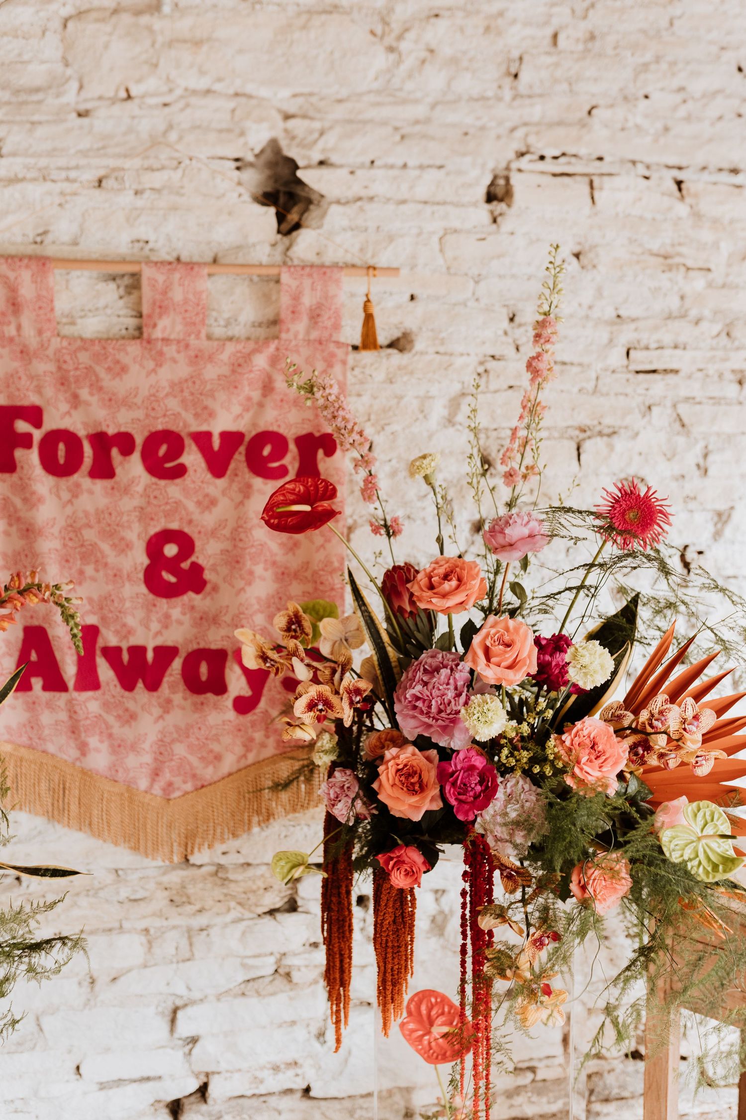 Rustic wall decorated with red 'Forever & Always' text and colorful floral arrangement featuring roses and tropical blooms.