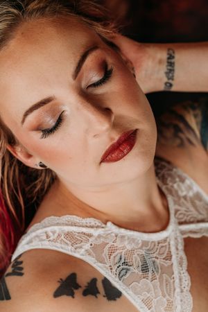 A close-up artistic portrait showing red lipstick and closed eyes against a warm background. Grand Rapids Nice & Naughty Store Boudoir Photo