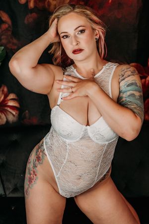 Woman in white lace lingerie poses against dark background with moody red lighting. Grand Rapids Nice and Naughty Store Boudoir Marathon