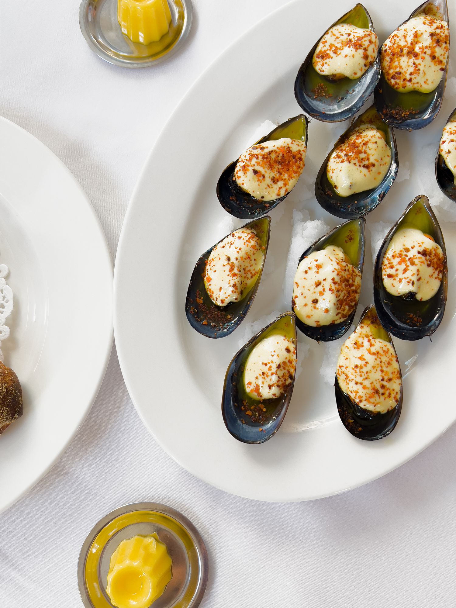 Fresh mussels arranged on white plates with lemon wedges and dipping sauce showcase an elegant seafood appetizer presentation.