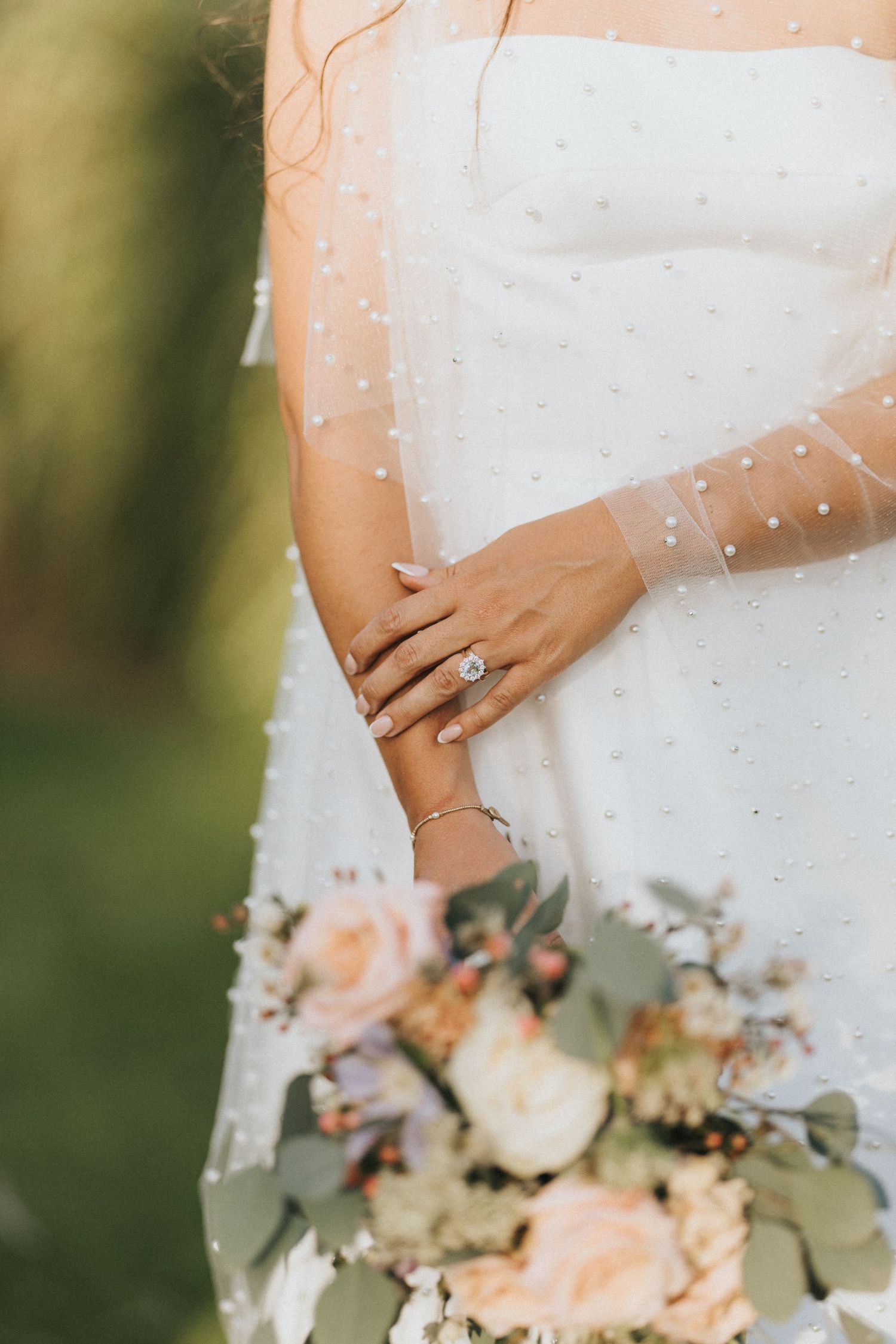 Close-up detail of wedding bouquet with peach roses and eucalyptus leaves, showing a diamond ring and white dress.
