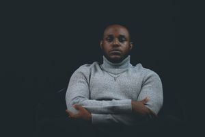 Person in gray turtleneck sweater poses with arms crossed against dark background.