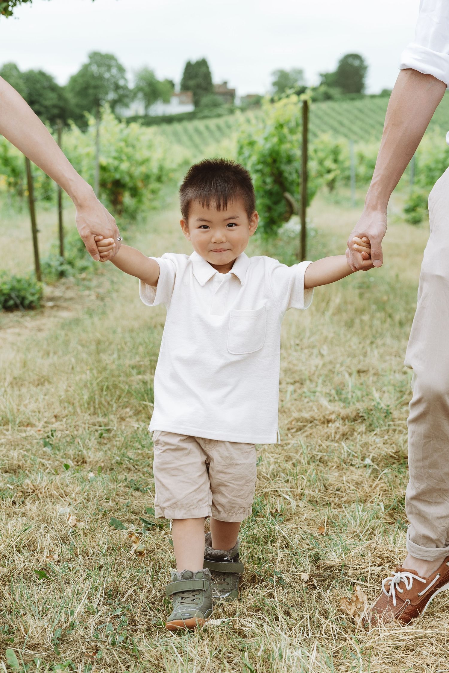 Children wearing white and beige outfits play together in a grassy field on a sunny day.