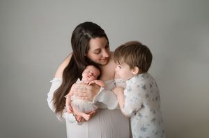 Mother and child share tender moments in soft natural light against a neutral grey wall background.