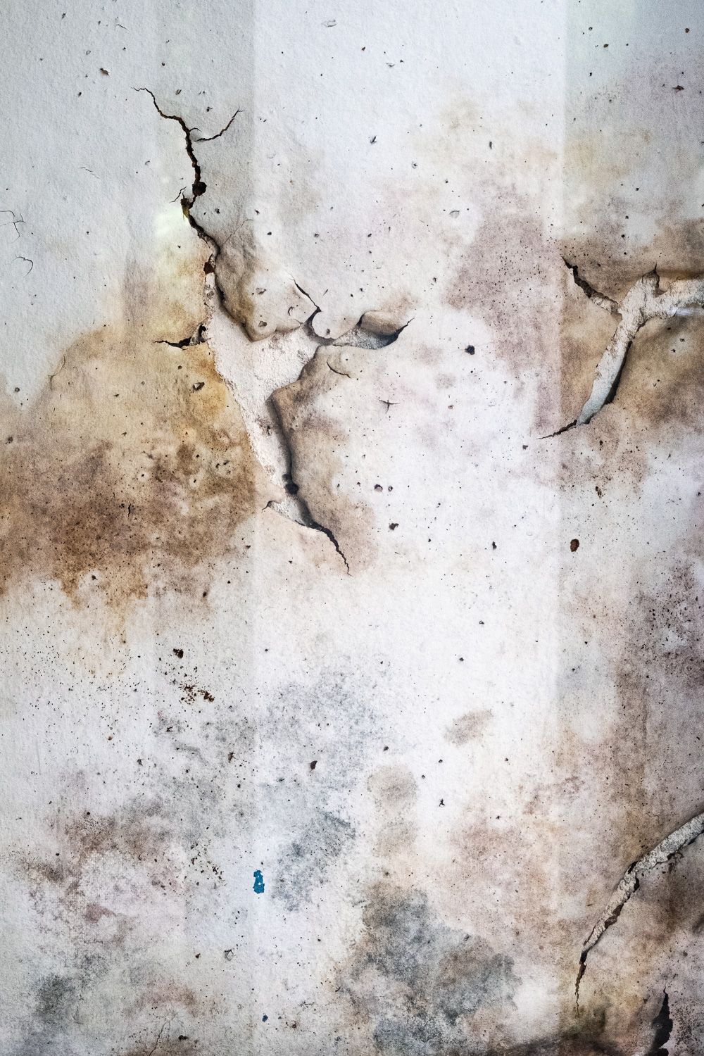 Abstract textured wall surface with peeling paint and brown stains creating a distressed, weathered appearance.