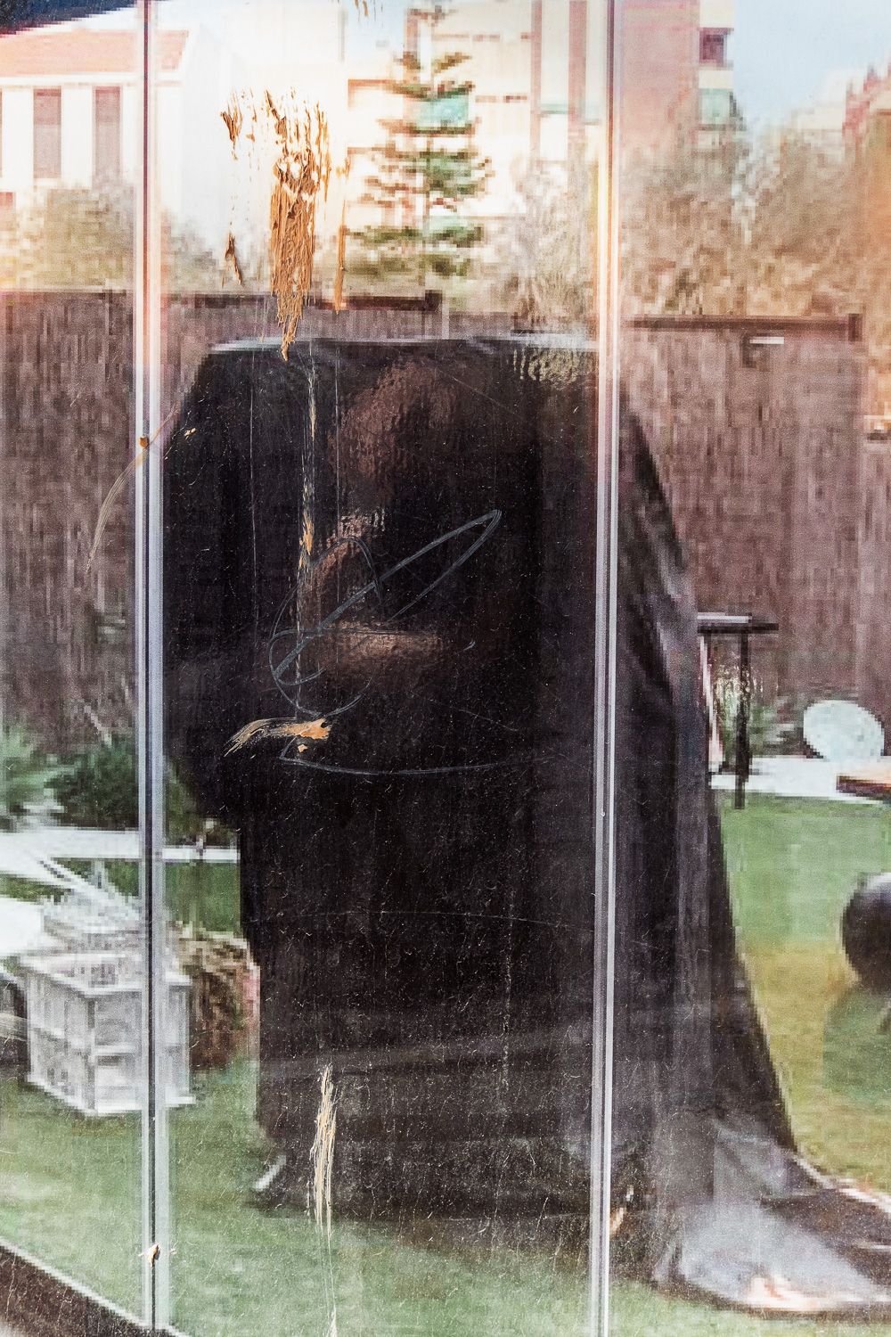 Large rectangular glass display case containing dark artifacts with transparent panels reflecting trees and grass outside.