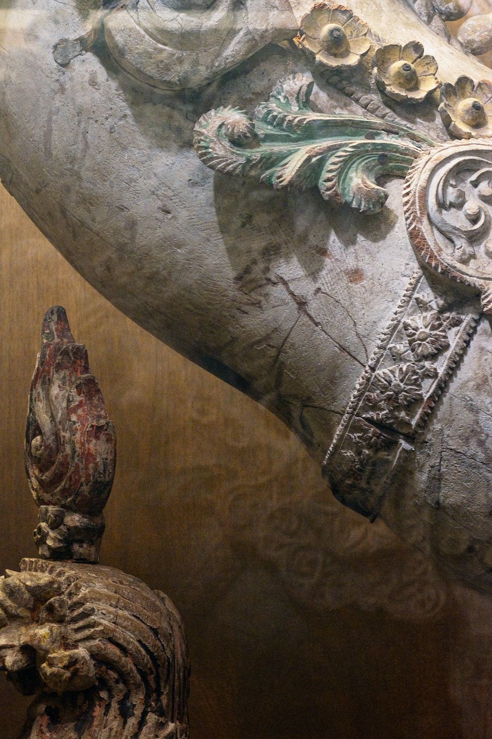 Ancient ceiling mural fragment showing ornate decorative patterns and flourishes against a dark background.
