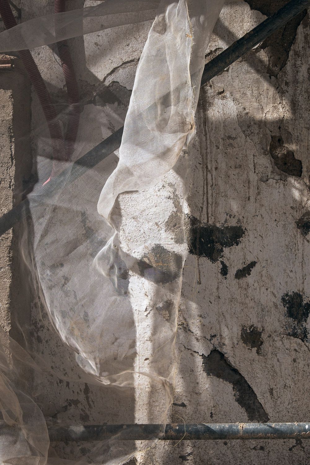 A tattered translucent plastic sheet hangs against a weathered concrete wall with dark shadows and marks.