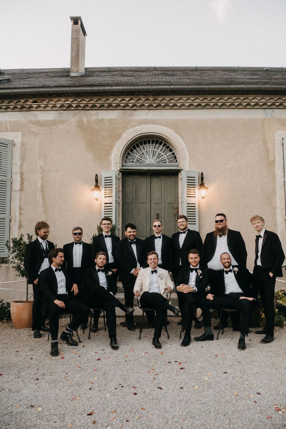 Wedding party members in formal black attire seated together on a stone patio for elegant group photo.