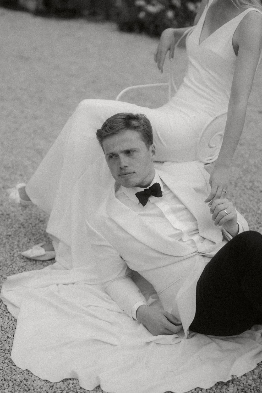 A bride in a white gown lays on gravel while posing for series of artistic black and white wedding photographs.