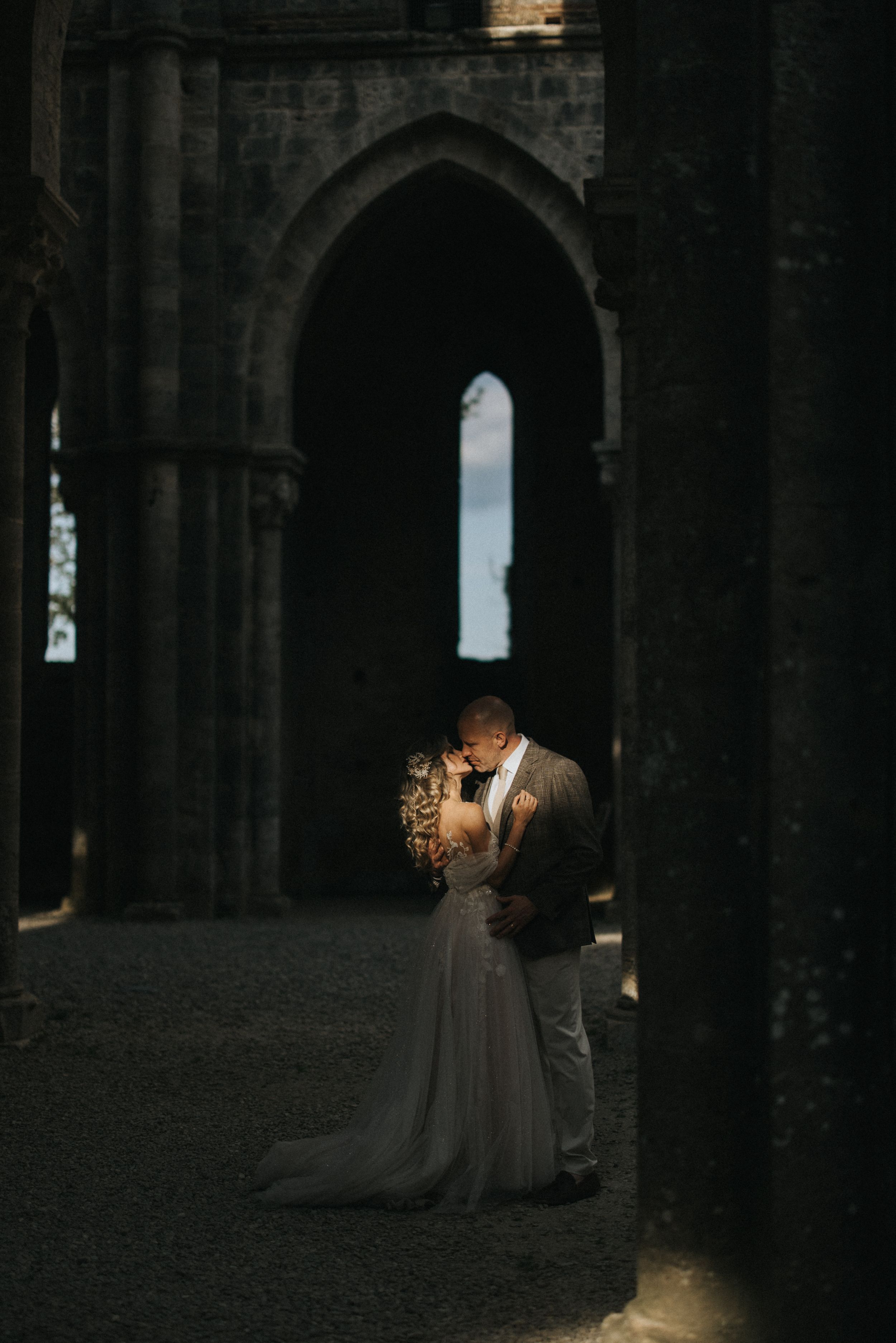 A couple embraces in a romantic kiss under a dramatic gothic stone archway at dusk. Captured by Lincolnshire photographers.