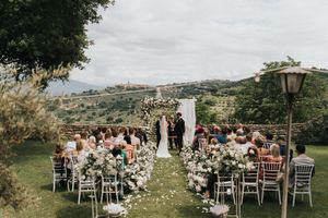 Outdoor wedding ceremony setup with white chairs overlooking an Italian scenic hillside landscape in natural sunlight.