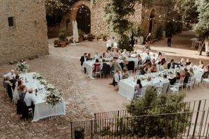 An elegant outdoor wedding reception setup in a rustic stone courtyard in Italy with tables decorated in white linens and flowers.