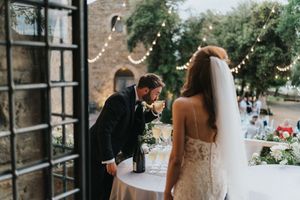 An intimate Italian wedding reception scene with twinkling lights and brick wall backdrop as couple shares quiet moment.