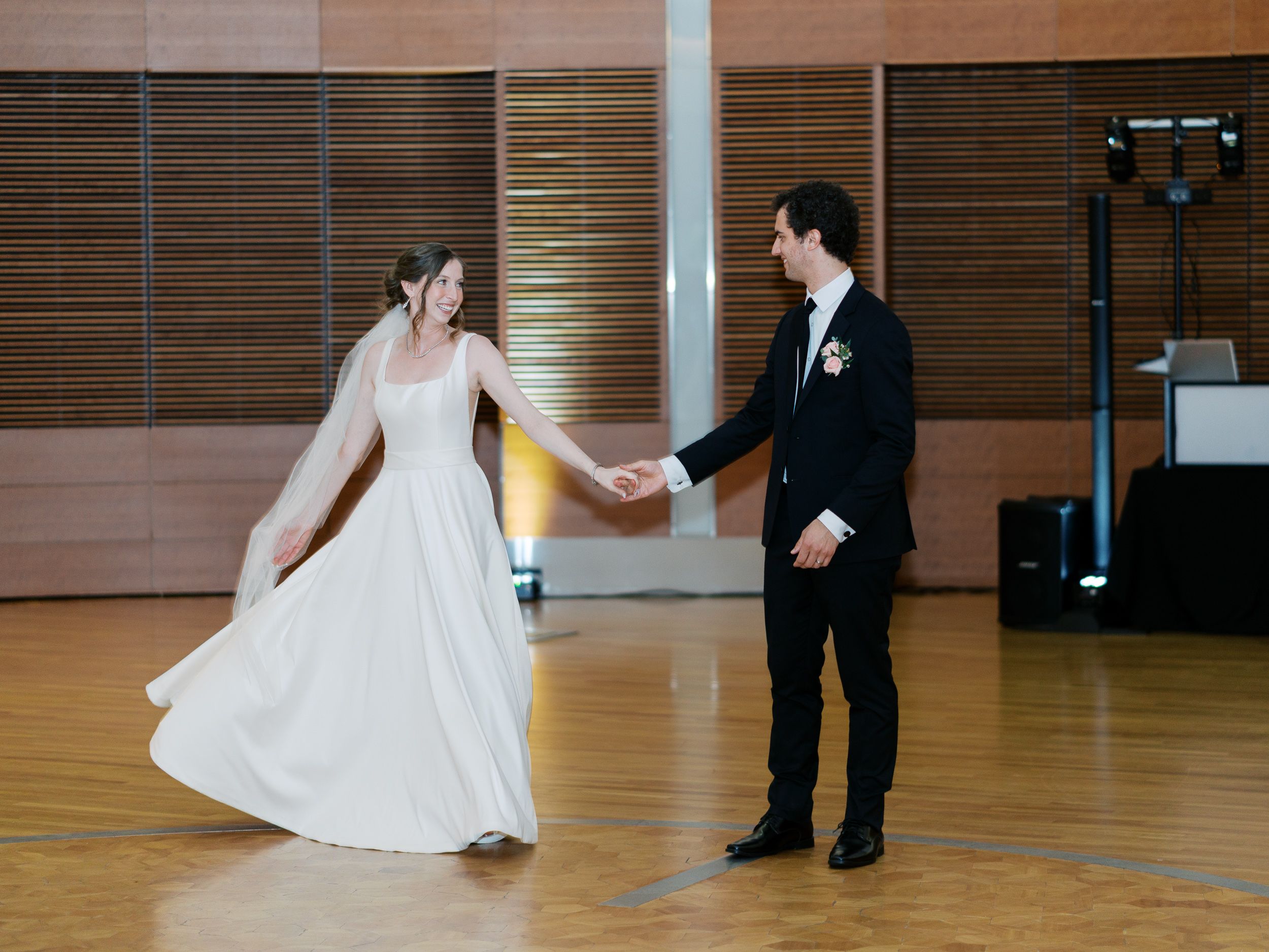 A couple performs their first dance in an elegant reception hall with wooden walls and polished hardwood floors.