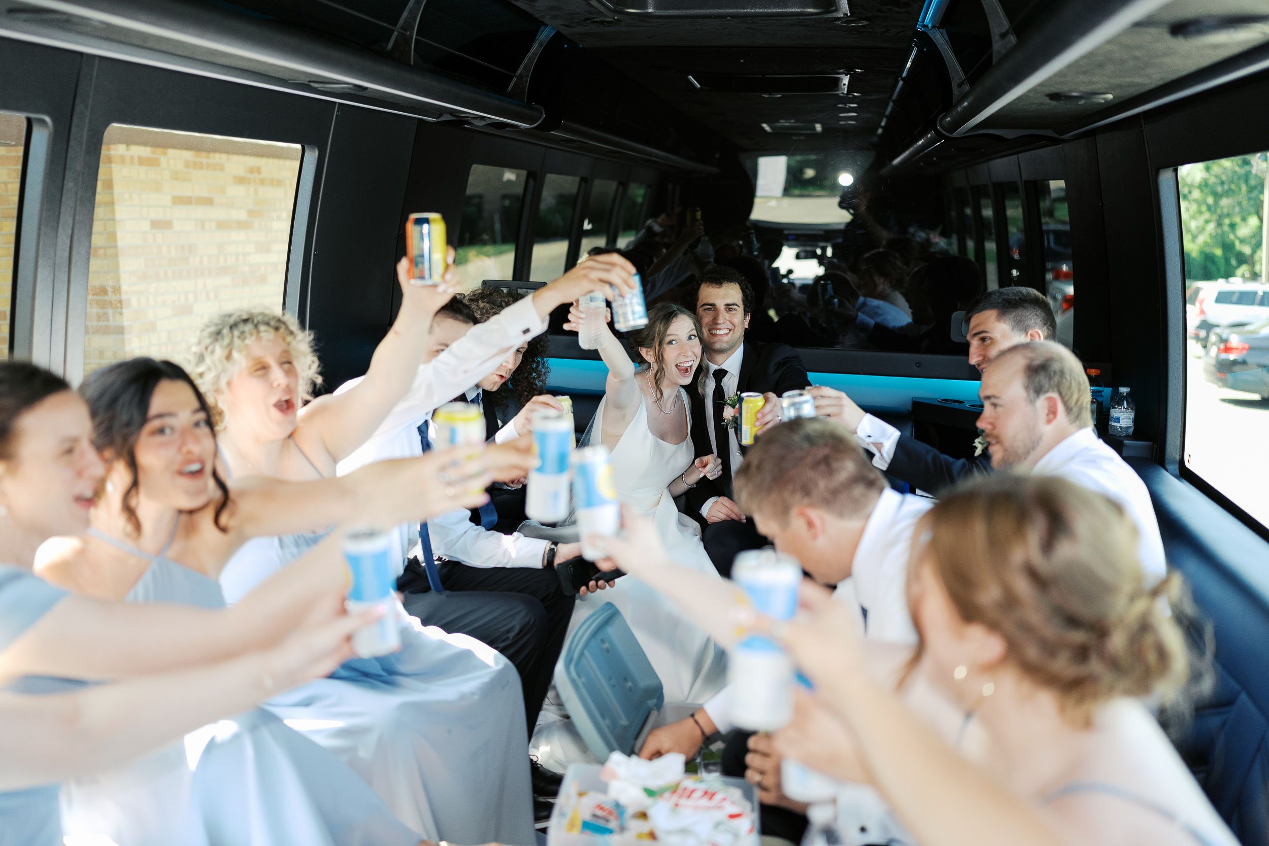 Wedding party celebrates with champagne toasts while riding together in a luxury party bus.