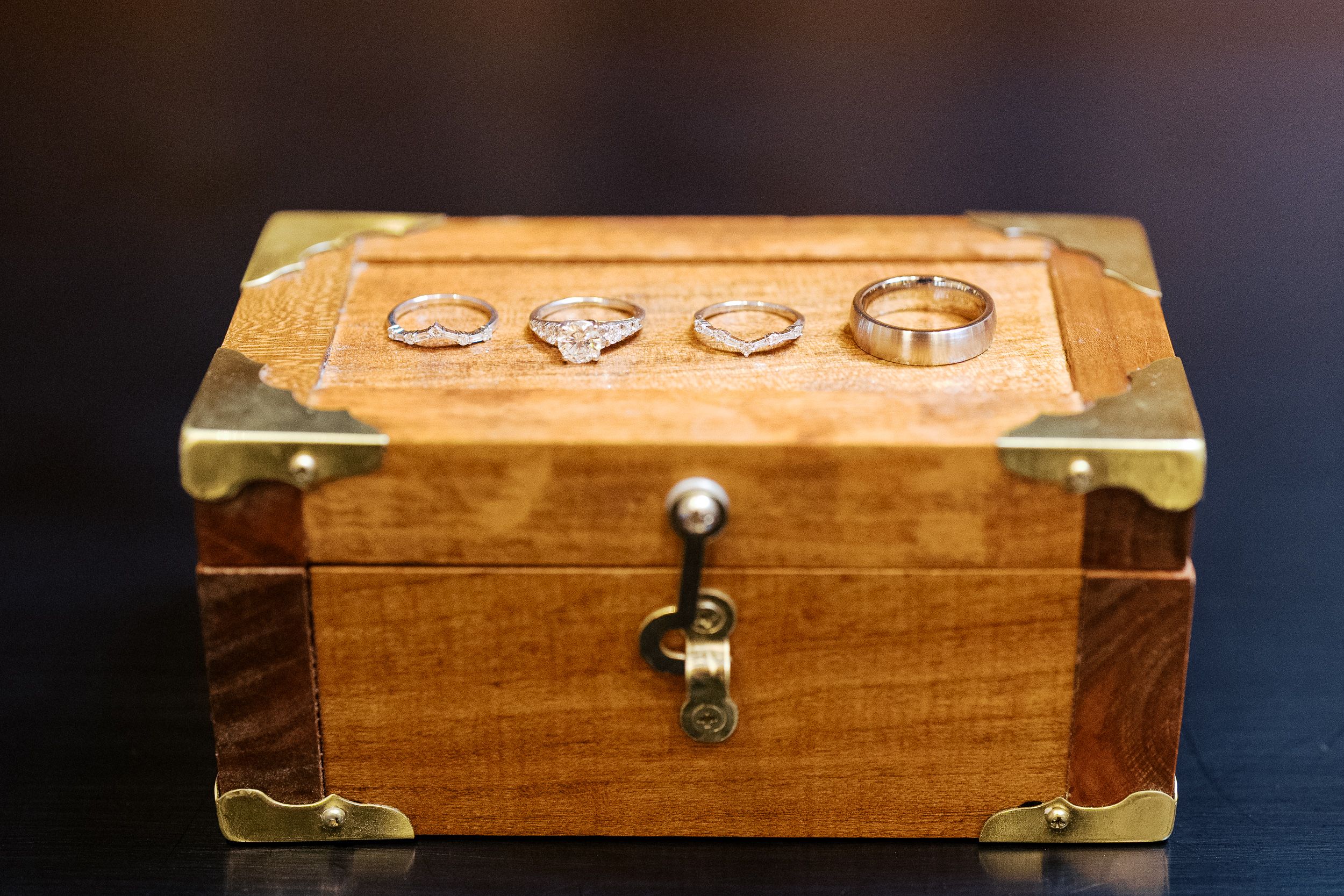 A vintage wooden jewelry box with brass corners and carved decorative details sits against a dark background.