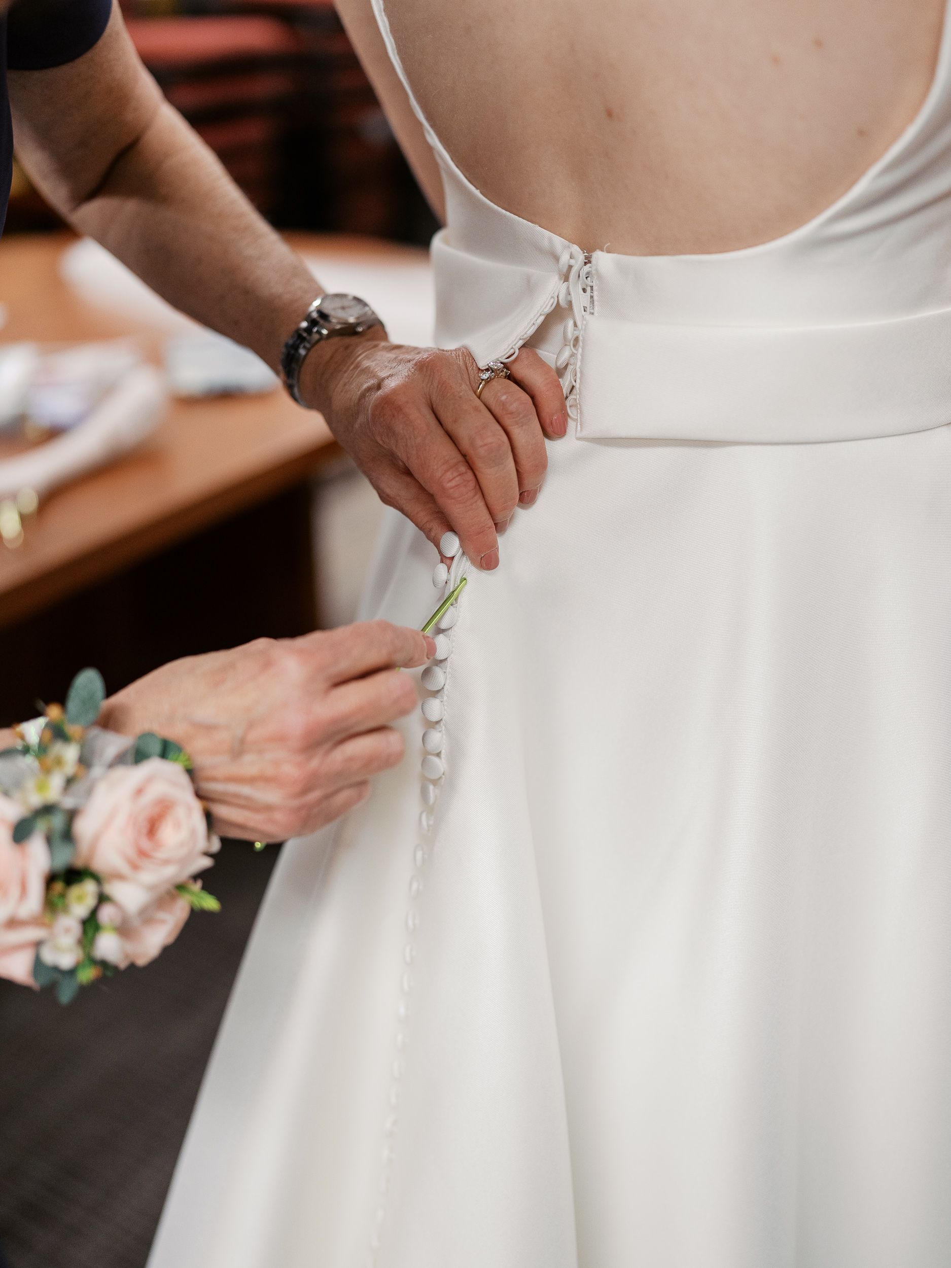 Row of wedding dress detail shots showing someone fastening buttons on elegant white bridal gown.