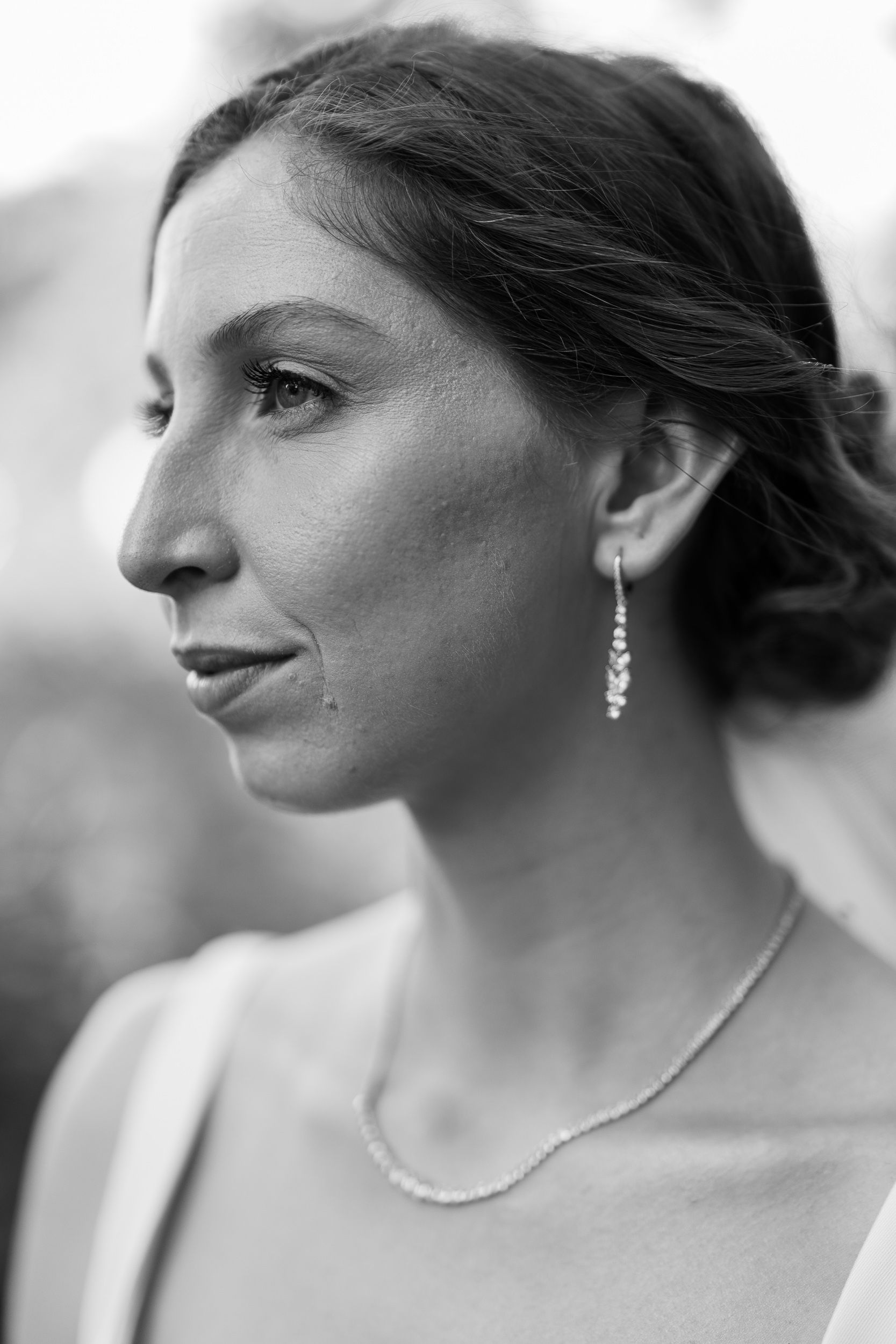 Elegant black and white portrait showing delicate jewelry and upswept hairstyle against a soft background.