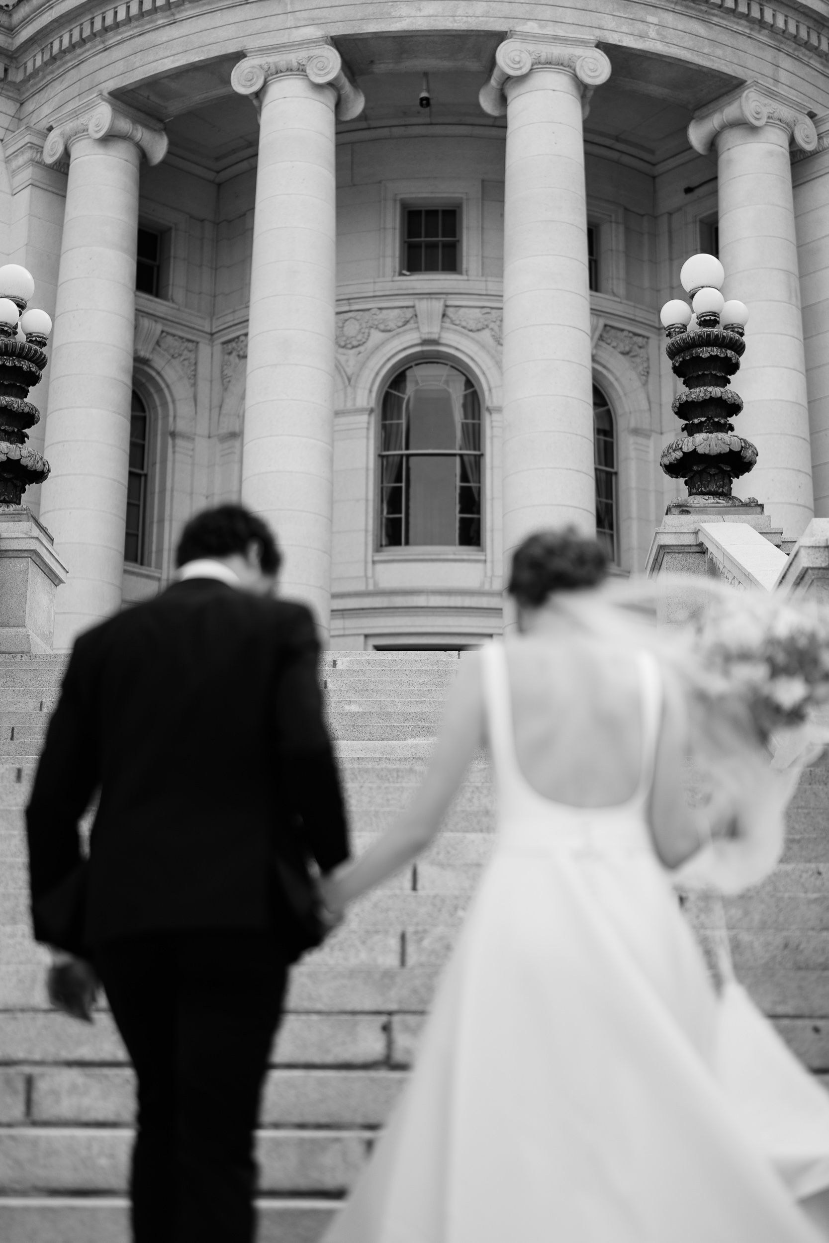 A bride and groom walk up grand marble steps at the Wisconsin State Capitol building in Madison.