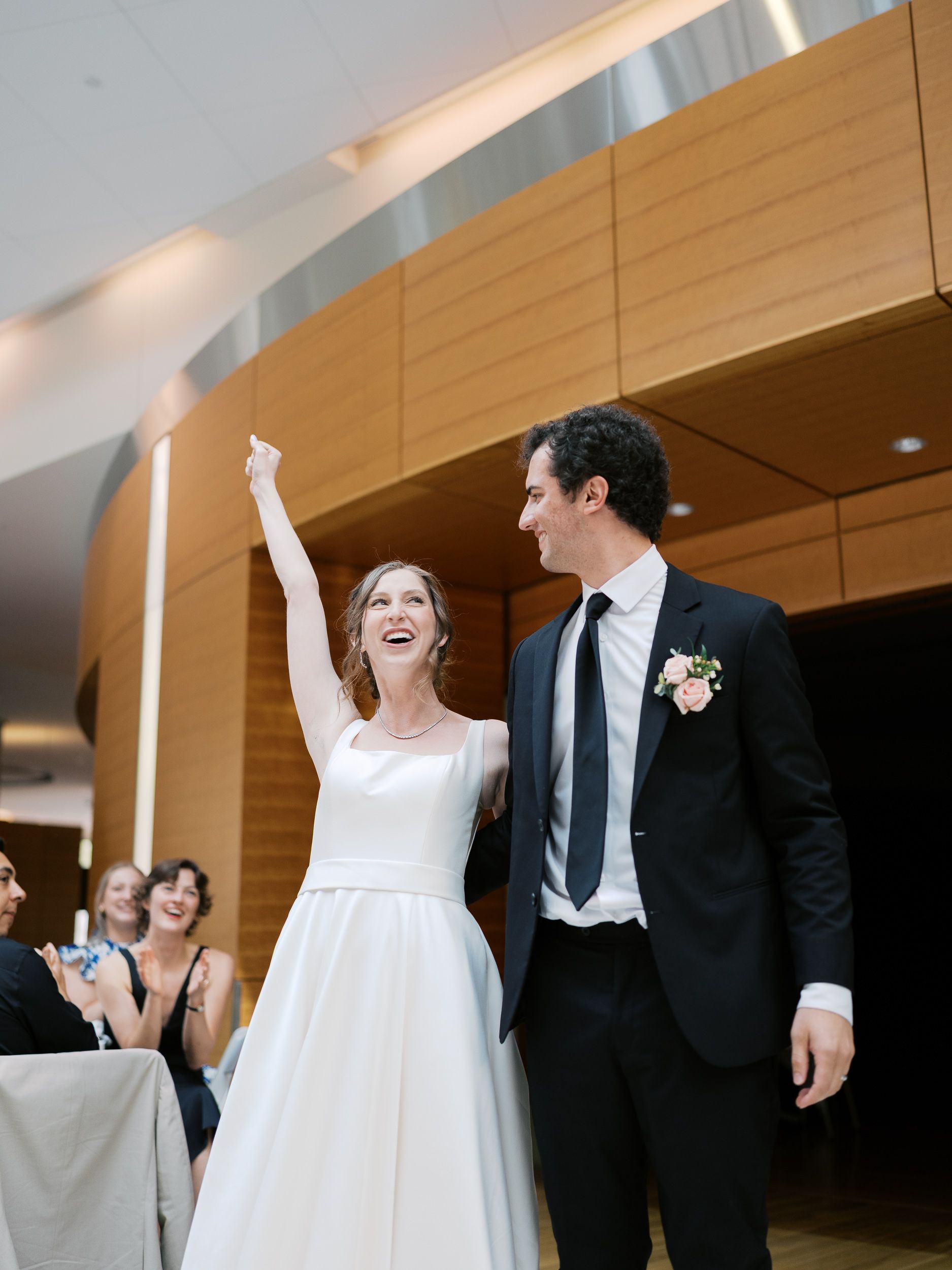A celebratory moment at a wedding reception shows an elegant couple in formal attire surrounded by guests.